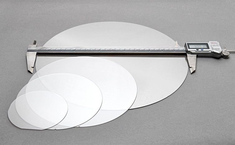 Four wafers and a set of calipers sit on a gray background. 