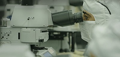 A lab worker at high-powered microscope representing Wolfspeed’s focus on innovation.