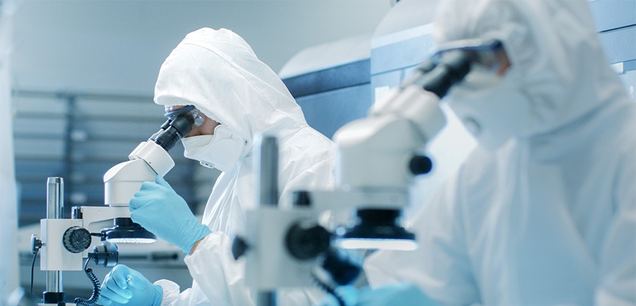 Two people in clean suits look into high powered microscopes, similar to how product quality testing is preformed at Wolfspeed.